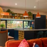 Seating area flowing into a blue bespoke kitchen with floating shelves